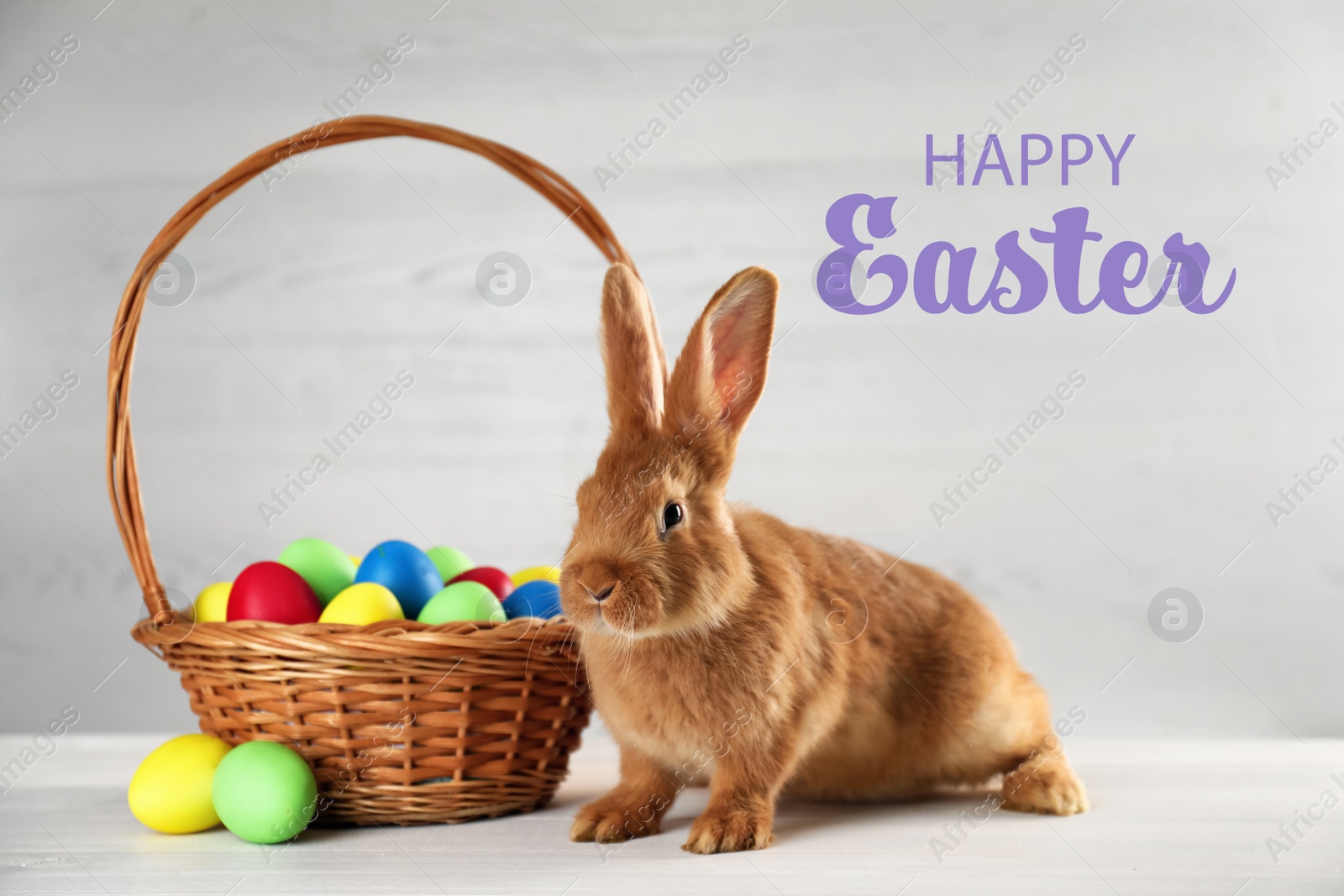 Image of Happy Easter! Cute bunny and wicker basket with dyed eggs on white table