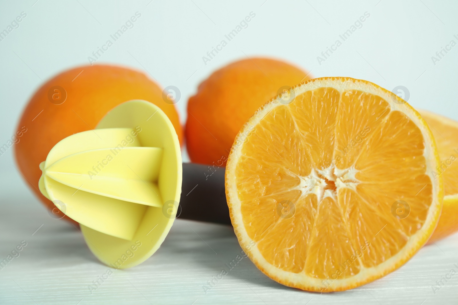 Photo of Fresh ripe oranges and reamer on white wooden table, closeup