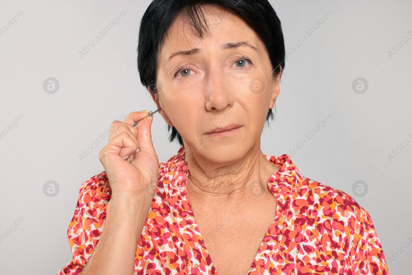 Photo of Senior woman cleaning ear with cotton swab on light grey background