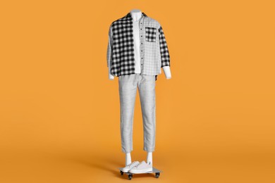 Photo of Male mannequin with sneakers dressed in white t-shirt, checkered shirt and pants on orange background. Stylish outfit