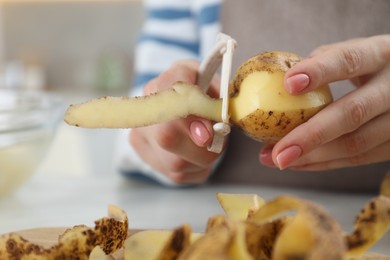 Photo of Woman peeling fresh potato at white table, closeup