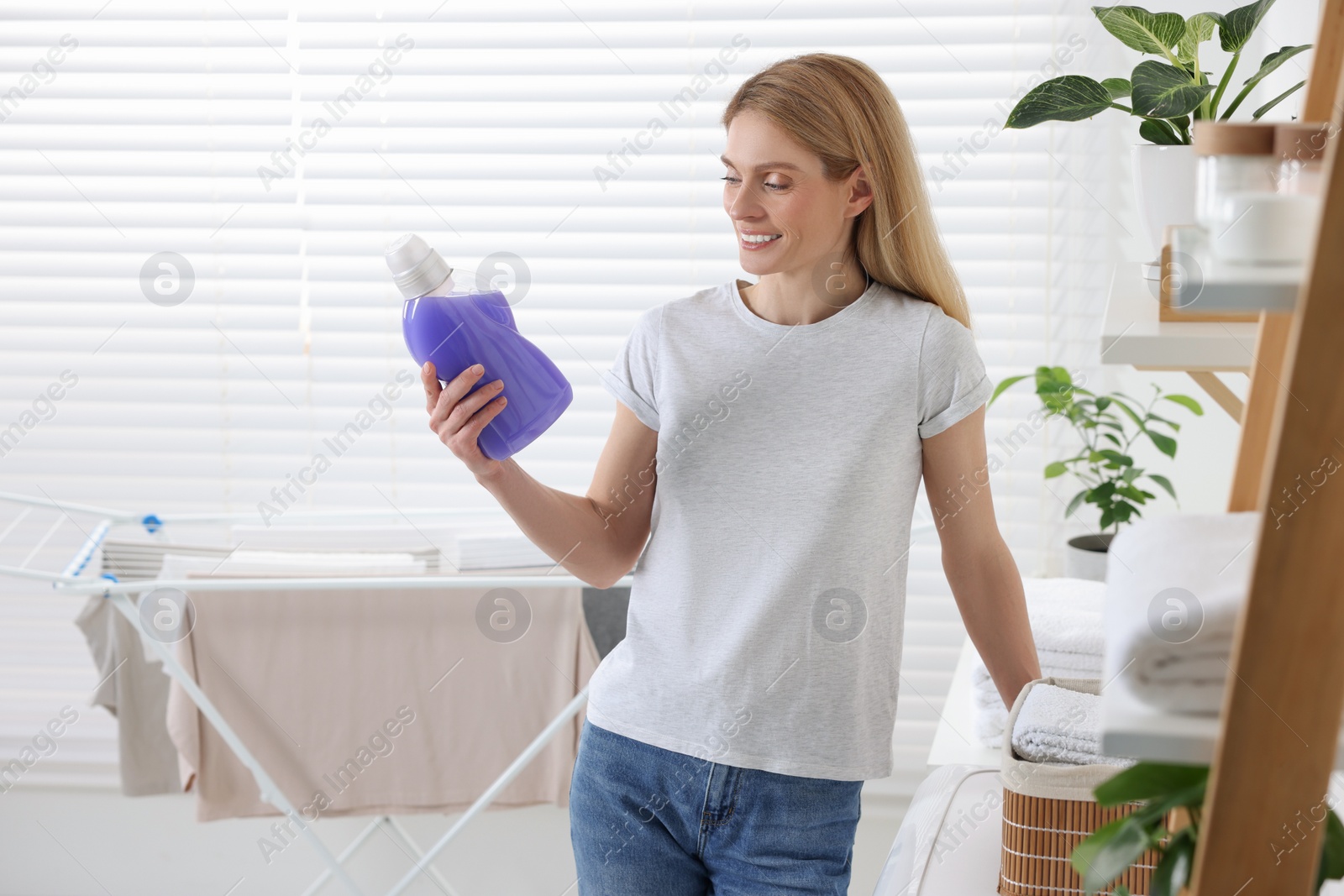 Photo of Woman holding fabric softener in bathroom, space for text