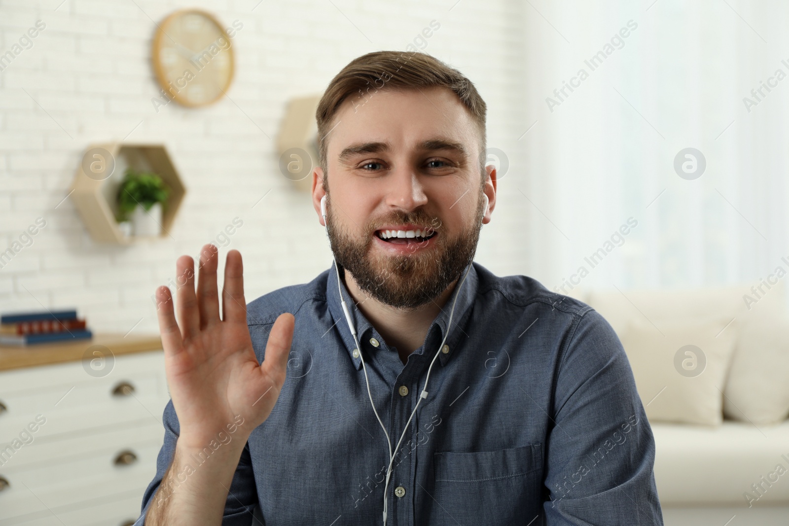 Photo of Young man with earphones holding online webinar indoors, view from webcam