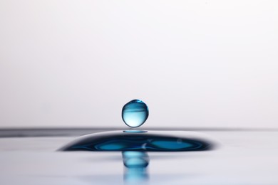 Photo of Drop falling into clear water on light background, closeup