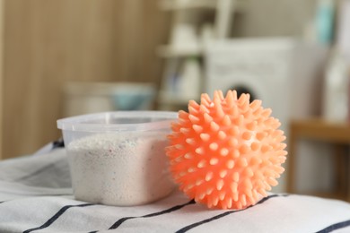 Photo of Orange dryer ball and detergent on clean clothing in laundry room, closeup