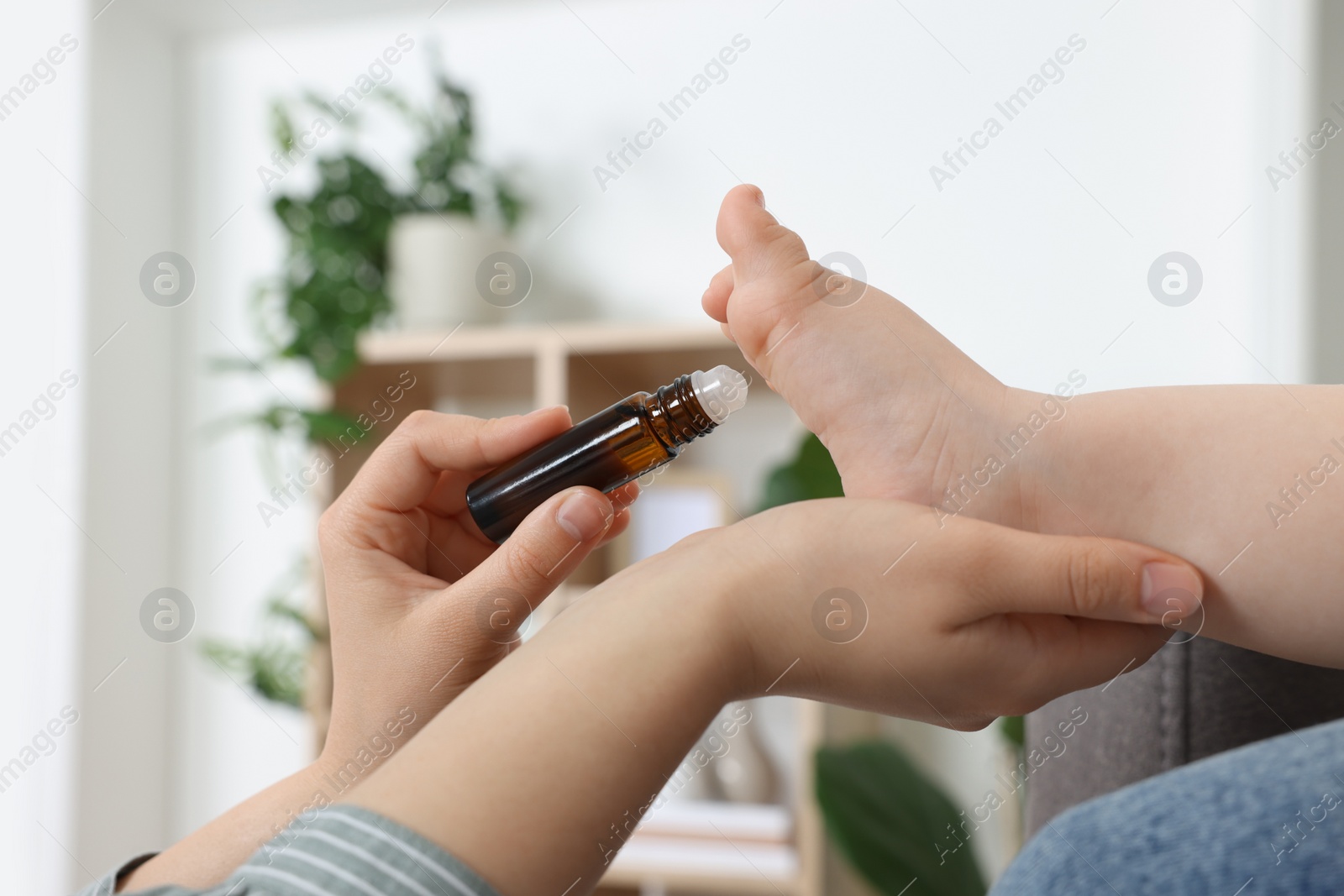 Photo of Mother applying essential oil from roller bottle onto her baby`s heel indoors, closeup