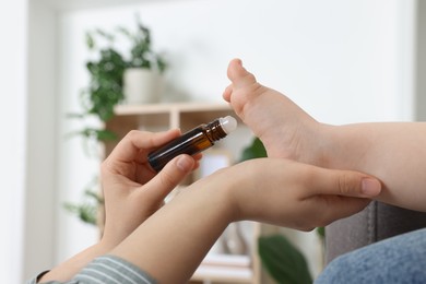 Mother applying essential oil from roller bottle onto her baby`s heel indoors, closeup