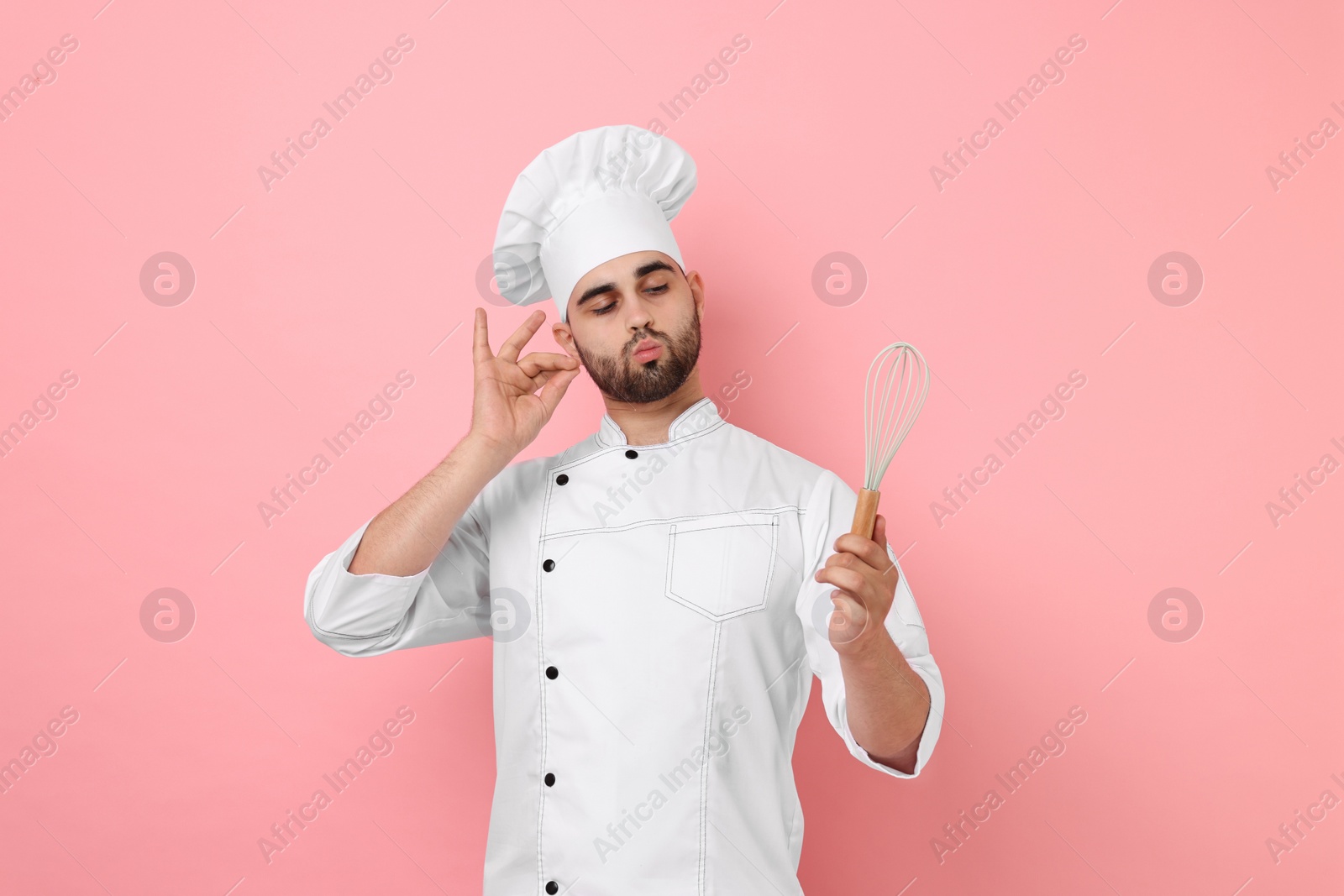 Photo of Professional chef holding whisk and showing perfect sign on pink background