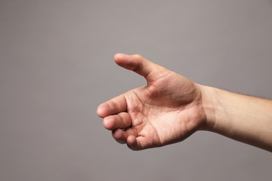 Man holding something in hand on grey background, closeup. Space for text