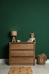 Modern wooden chest of drawers with lamp and toy near green wall indoors
