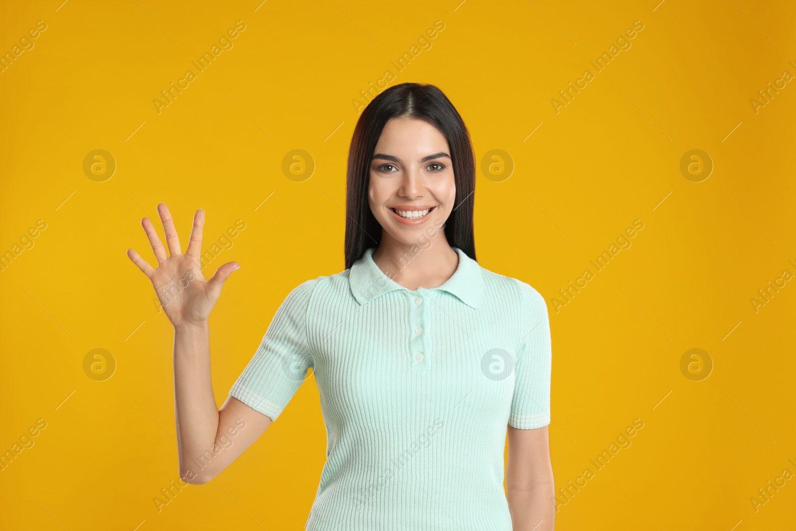 Photo of Woman showing number five with her hand on yellow background