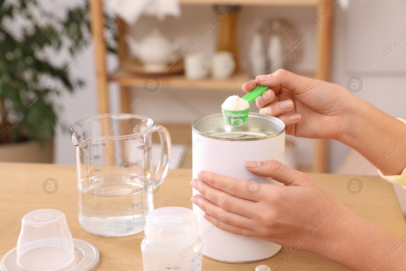 Photo of Woman preparing infant formula at table indoors, closeup. Baby milk