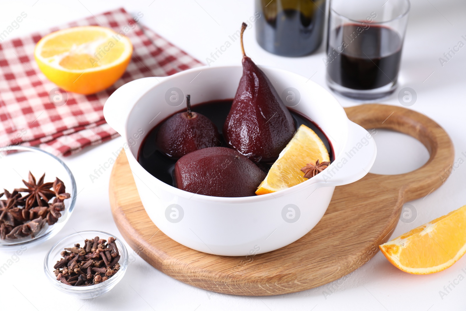 Photo of Tasty red wine poached pears in pot, orange and spices on white table, closeup