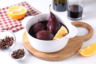 Tasty red wine poached pears in pot, orange and spices on white table, closeup