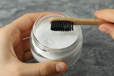 Photo of Young woman with toothbrush and jar of baking soda at grey table, closeup