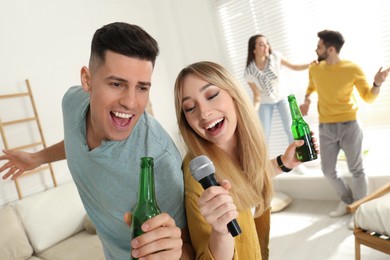 Photo of Happy couple singing karaoke with friends at home