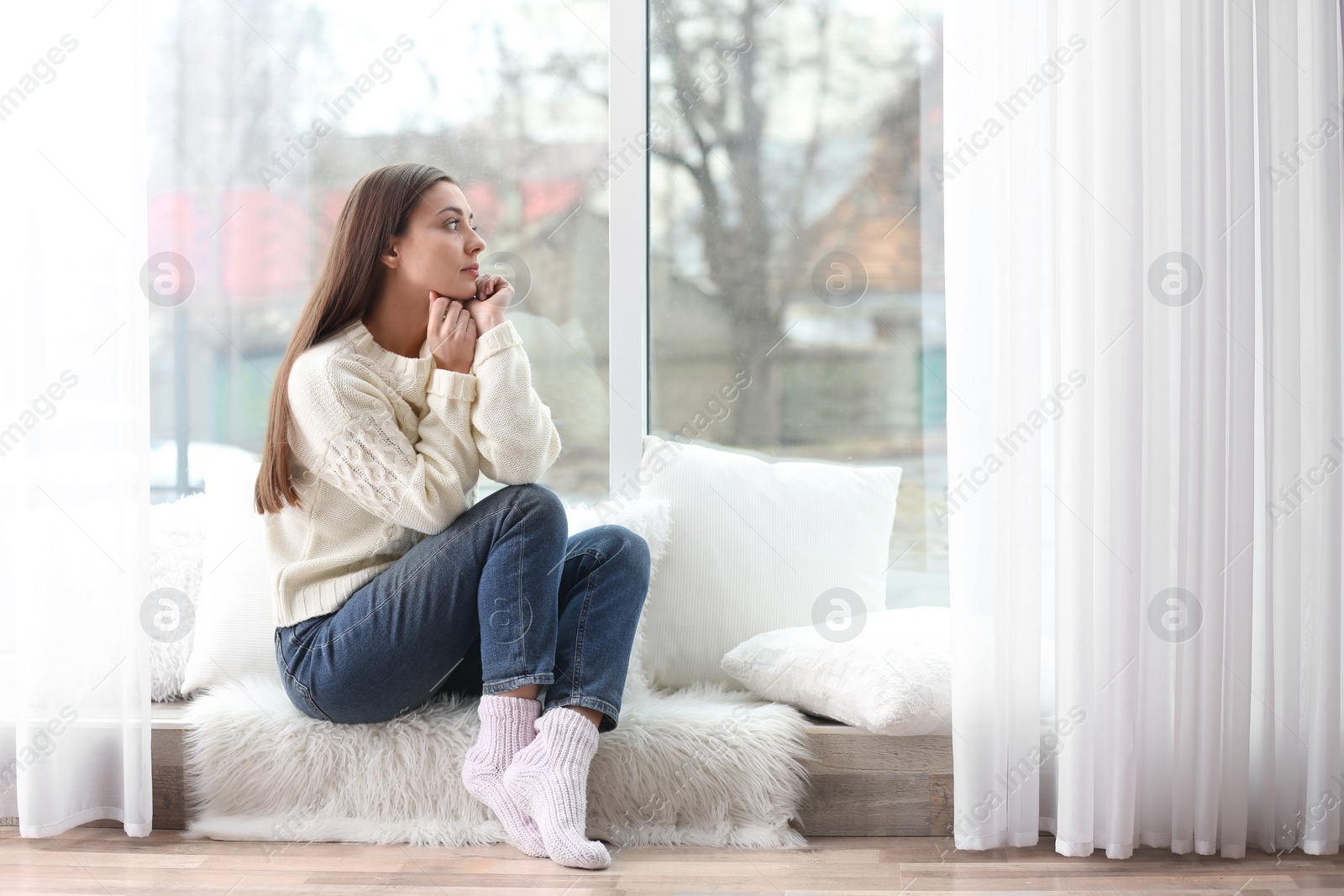 Photo of Young woman in sweater sitting near window indoors
