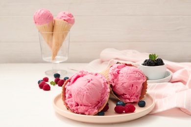 Delicious pink ice cream in wafer cones with berries on white wooden table