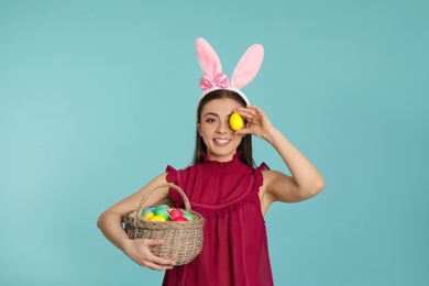 Photo of Beautiful woman in bunny ears headband with Easter eggs on color background