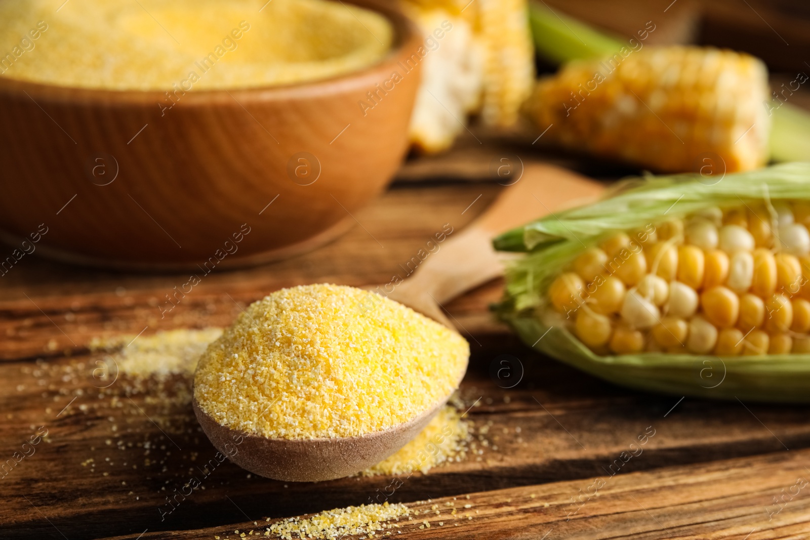 Photo of Cornmeal in spoon on wooden table, closeup