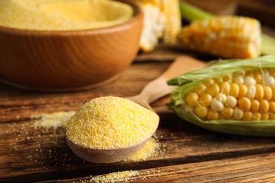 Photo of Cornmeal in spoon on wooden table, closeup