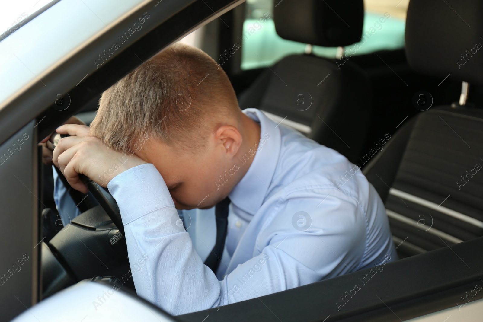 Photo of Tired young man sleeping on steering wheel in his car