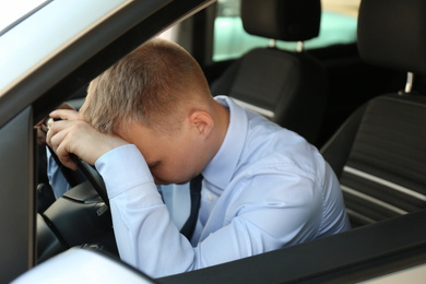 Tired young man sleeping on steering wheel in his car