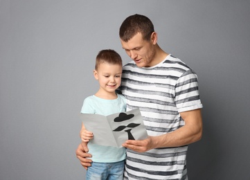 Photo of Little boy greeting his father with Father's Day on grey background