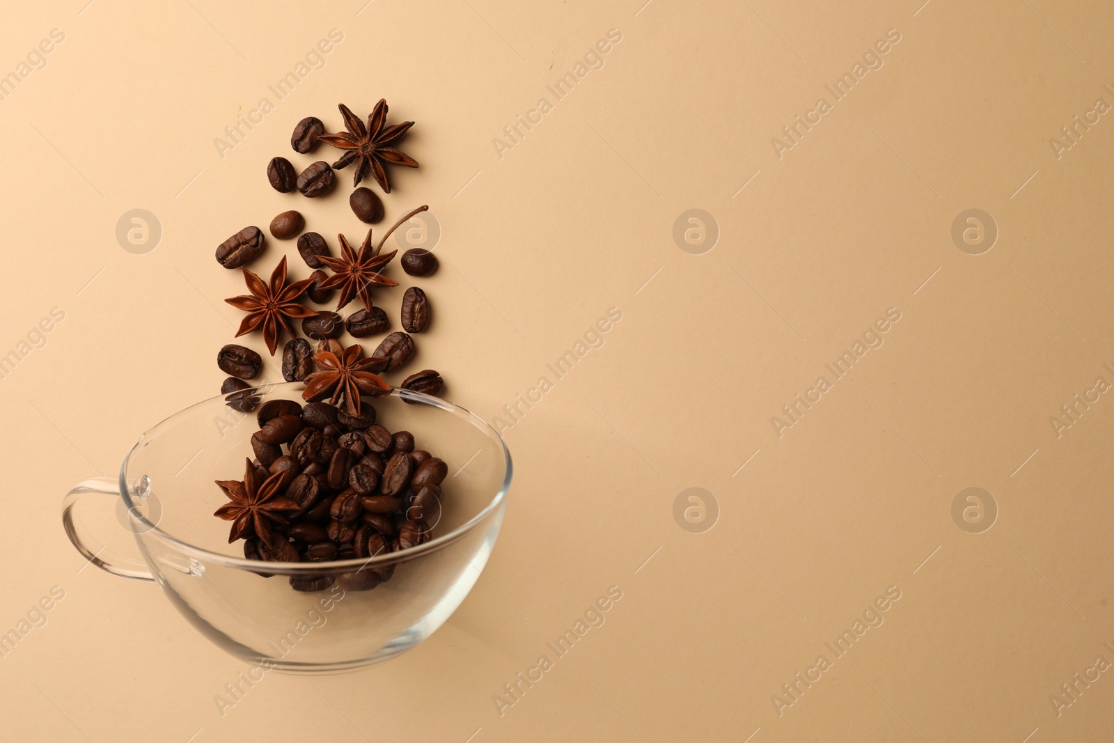 Photo of Coffee beans and anise stars falling into glass cup on beige background, flat lay. Space for text