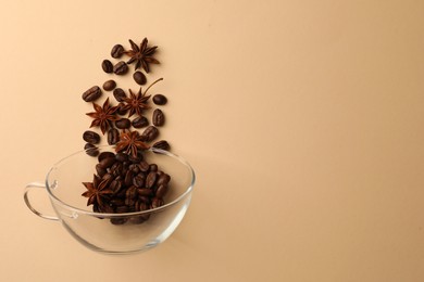 Photo of Coffee beans and anise stars falling into glass cup on beige background, flat lay. Space for text