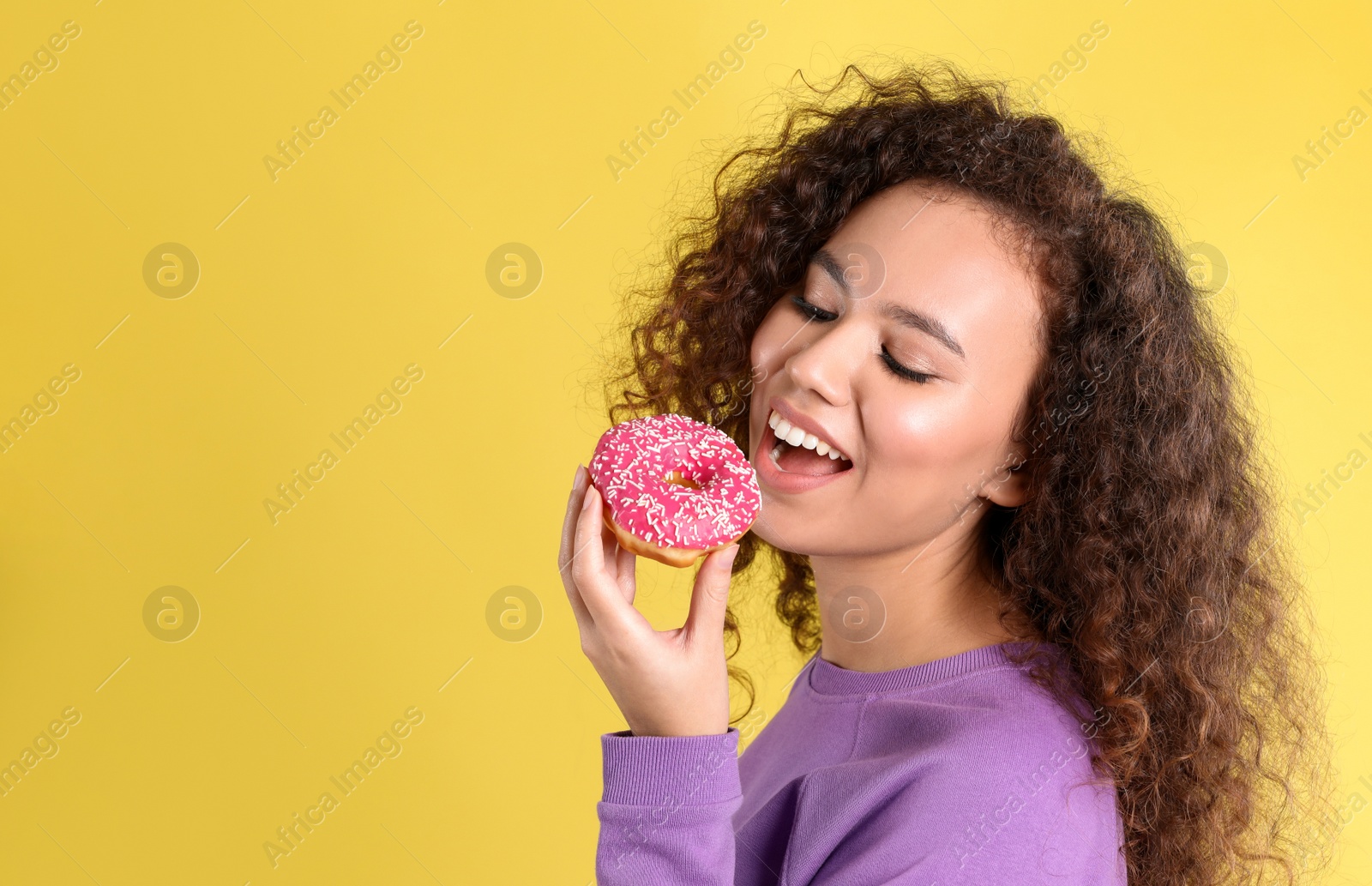 Photo of Beautiful African-American woman with donut on yellow background