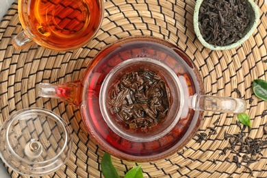 Photo of Teapot with hot aromatic tea on wicker mat, top view