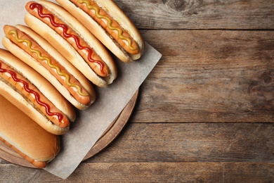 Photo of Tasty fresh hot dogs on wooden table, top view. Space for text