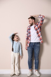 Photo of Father and daughter comparing their heights near beige wall indoors