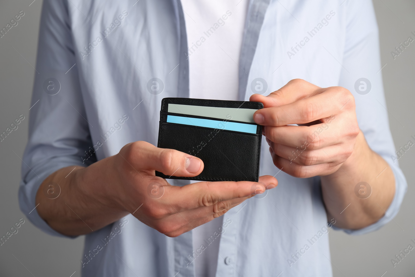 Photo of Man holding leather business card holder with cards on grey background, closeup