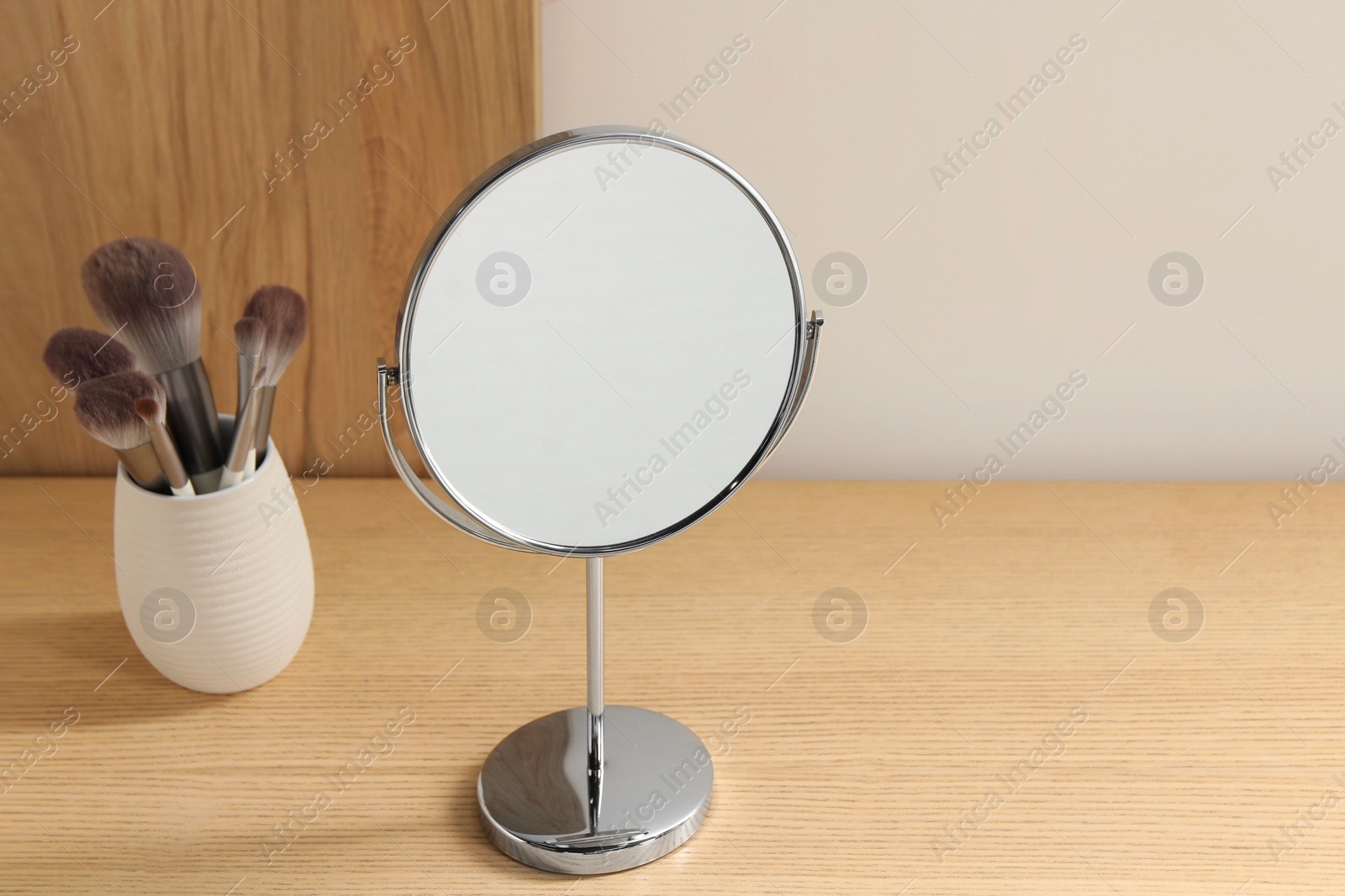 Photo of Mirror and makeup brushes on wooden dressing table in room. Space for text