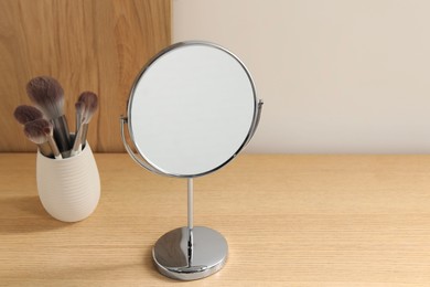 Mirror and makeup brushes on wooden dressing table in room. Space for text