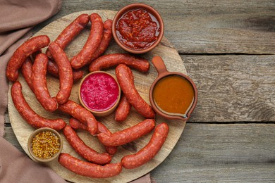 Photo of Delicious sausages, ketchup, mustard and horseradish on wooden table, top view. Space for text
