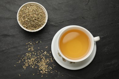 Photo of Aromatic fennel tea in cup and seeds on black table, flat lay