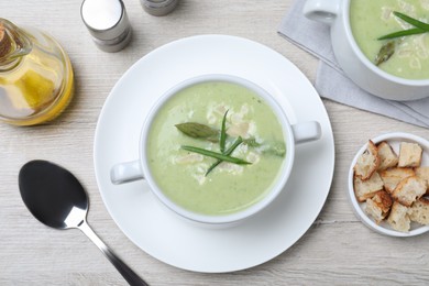 Delicious asparagus soup with green onion served on white wooden table, flat lay