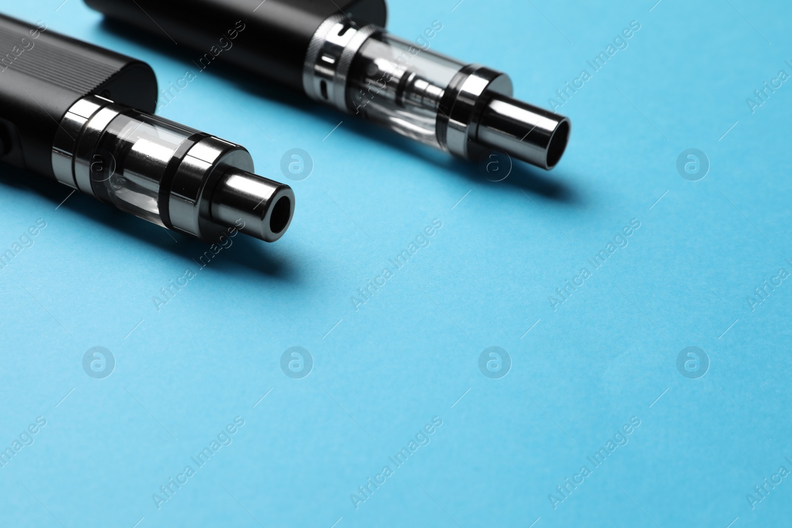 Photo of Two electronic cigarettes on light blue background, closeup. Space for text