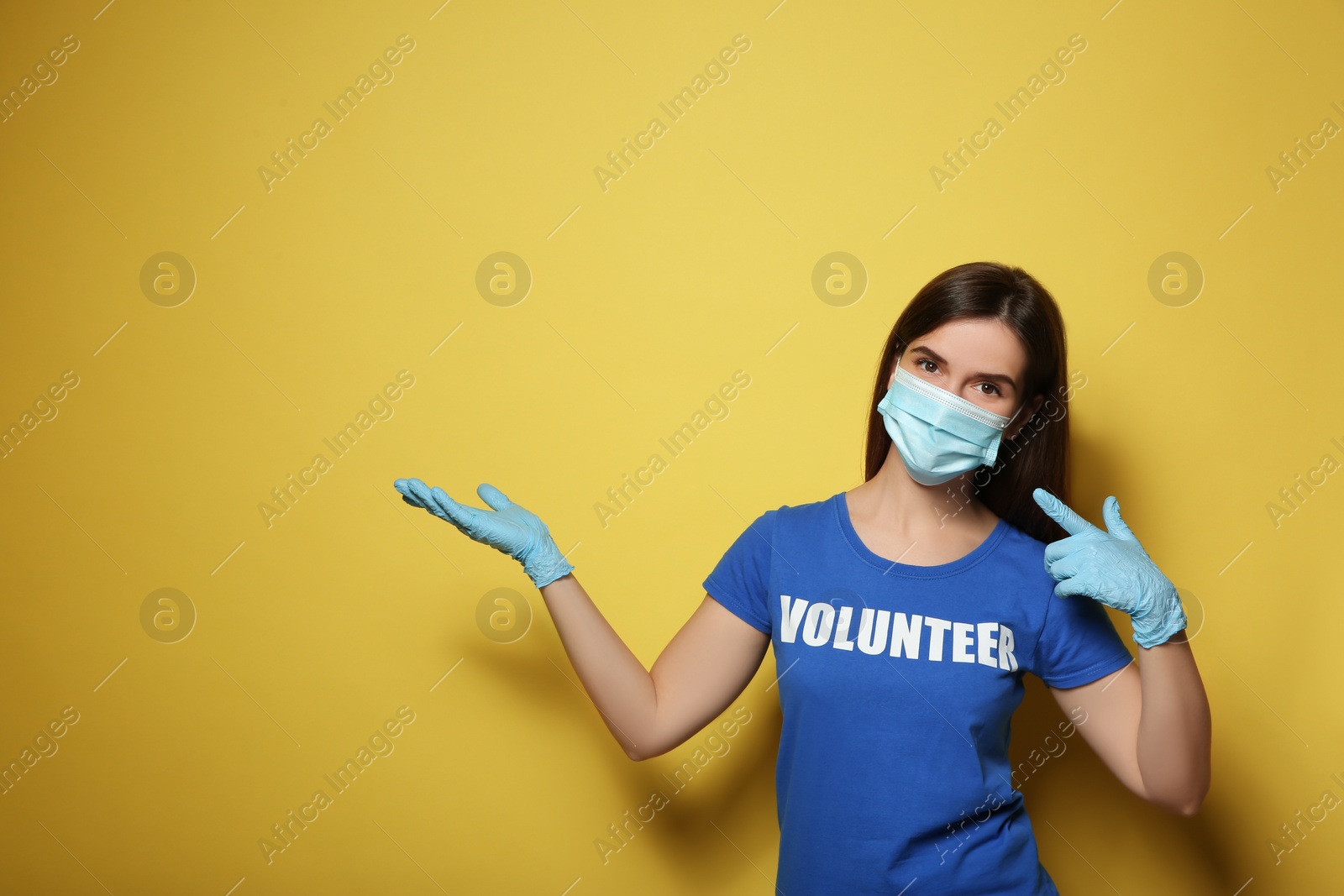 Photo of Female volunteer in mask and gloves on yellow background, space for text. Protective measures during coronavirus quarantine