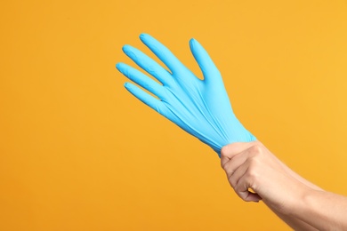 Photo of Doctor wearing medical gloves on yellow background, closeup. Space for text
