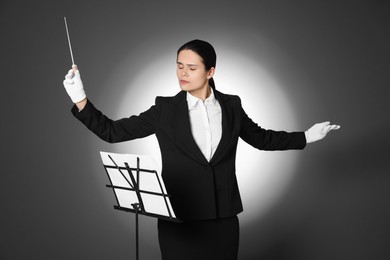 Professional conductor with baton and note stand on grey background