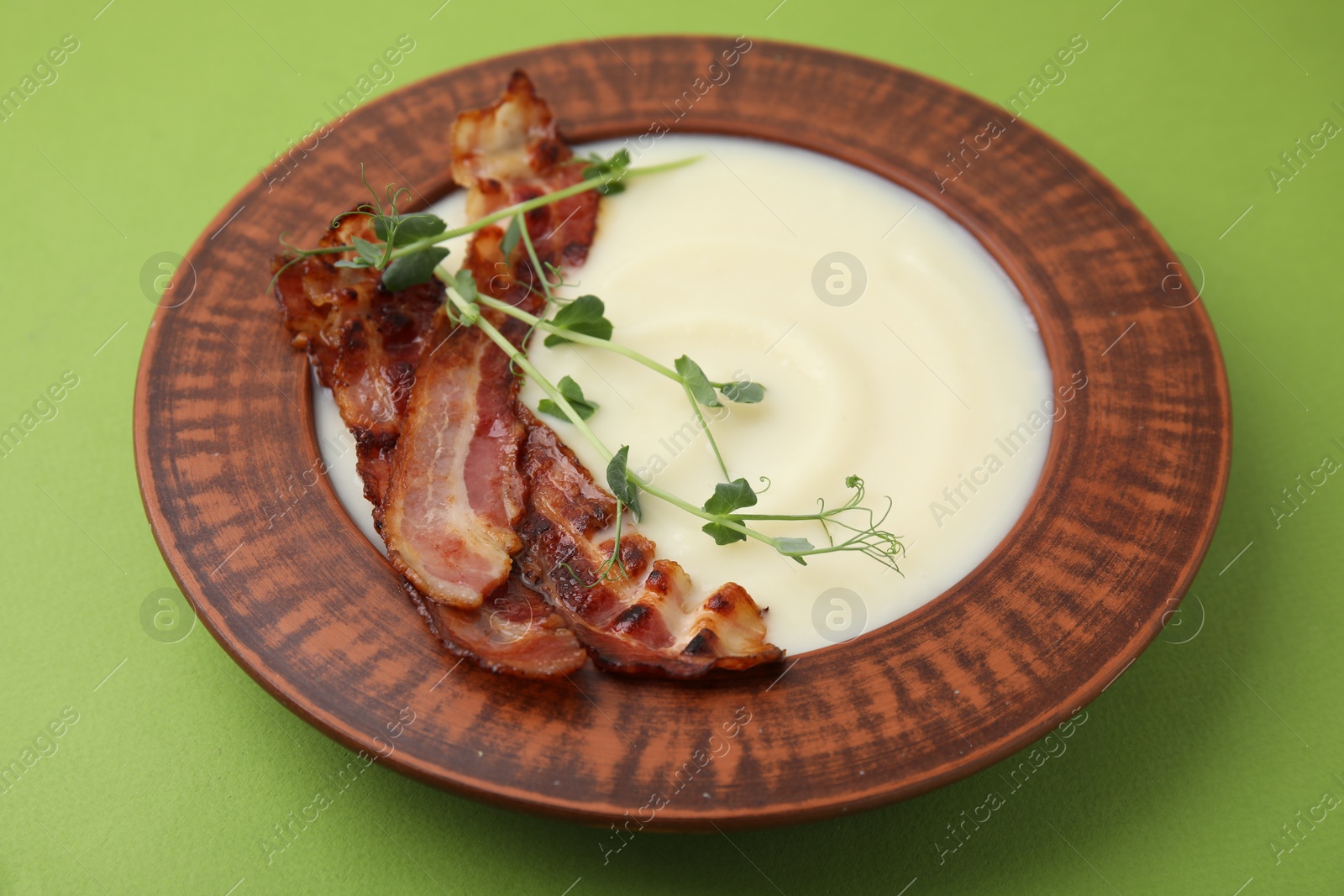 Photo of Delicious potato soup with bacon and microgreens in bowl on green table, closeup