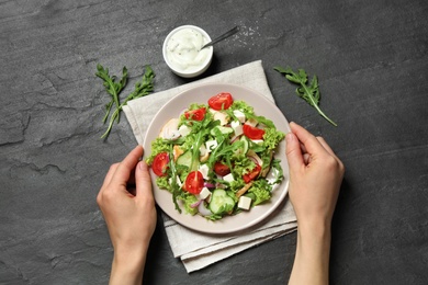 Photo of Woman holding plate with delicious arugula salad at black table, top view