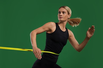 Photo of Athletic woman exercising with elastic resistance band on green background