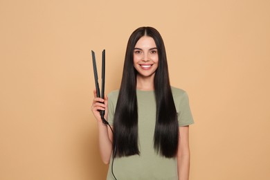 Photo of Beautiful happy woman with hair iron on beige background