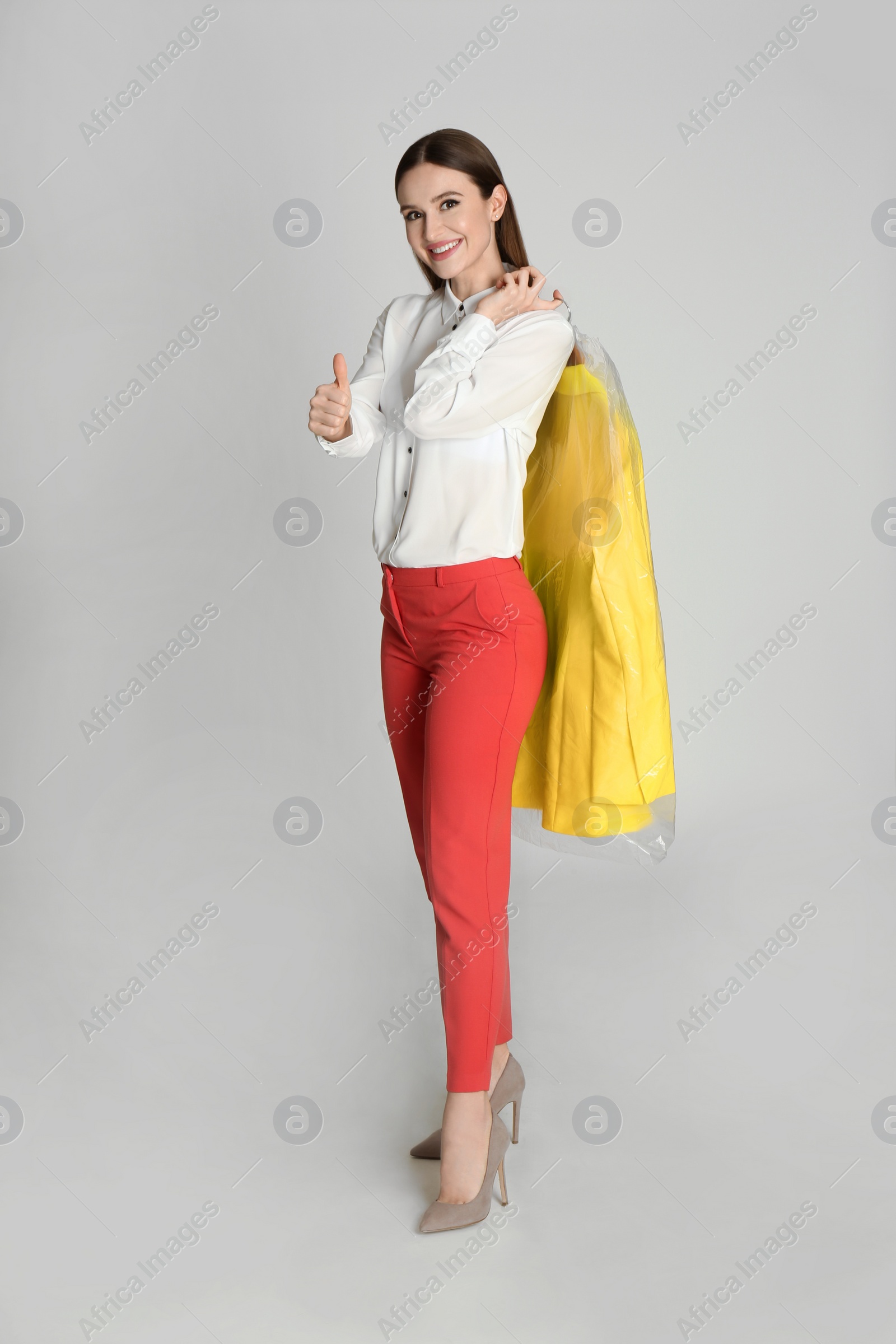 Photo of Young woman holding hanger with jacket on light grey background. Dry-cleaning service