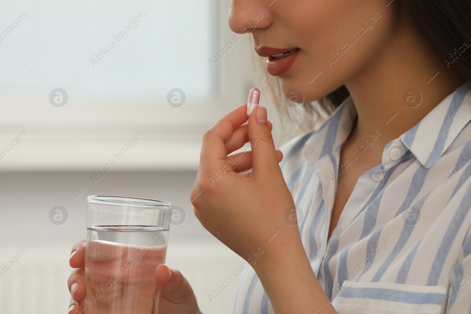 Photo of Young woman with glass of water taking dietary supplement pill indoors, closeup